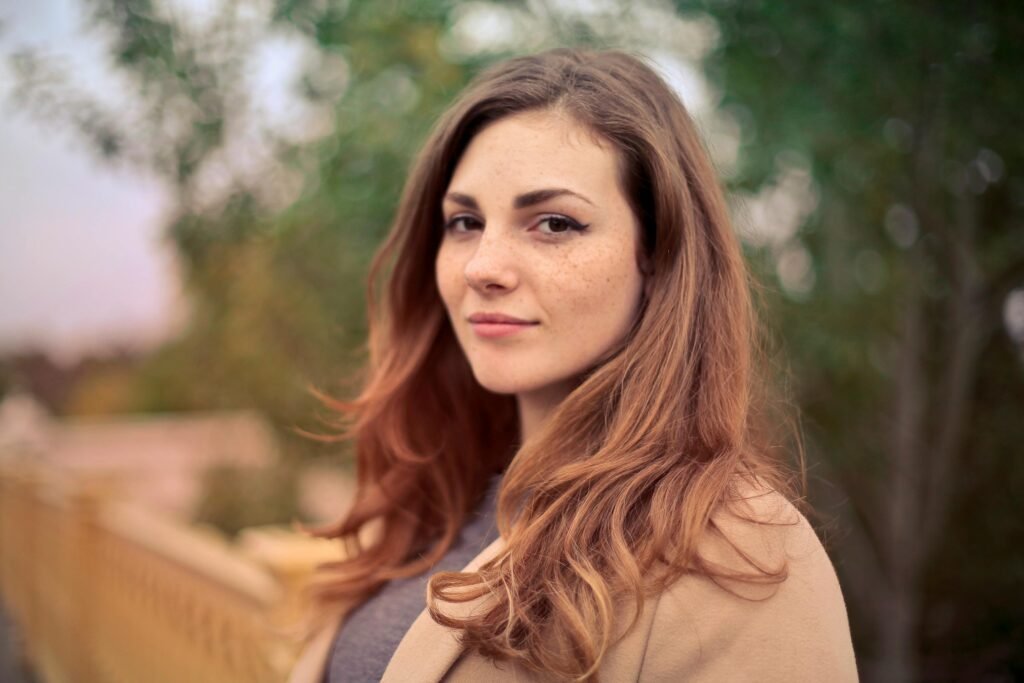 A young woman with long hair smiles confidently for an outdoor portrait session.